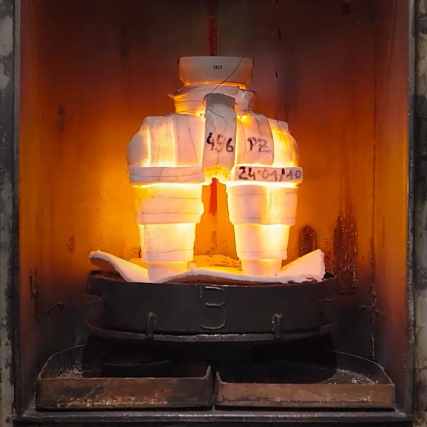 The image shows a wax model covered with various layers of ceramic powder and liquid inside an oven. This process allows the wax to melt out, leaving behind the actual casting mold.