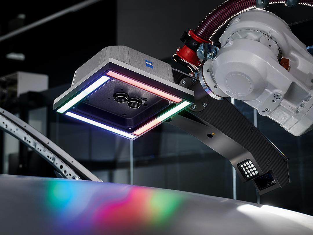 A robotic arm equipped with a ZEISS 3D scanning sensor hovers over a metallic surface, illuminated by multicolored LED lights.