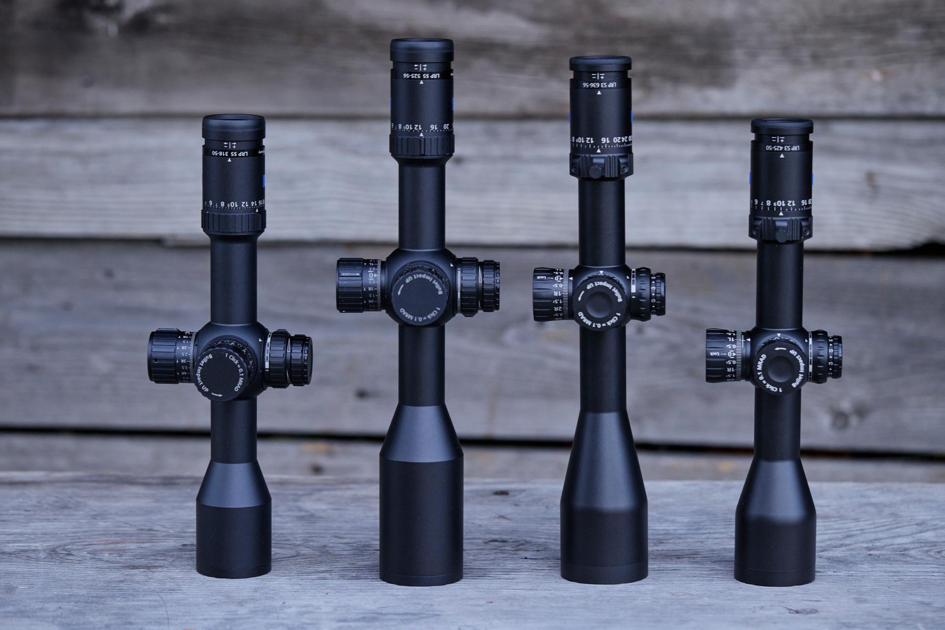 Four ZEISS riflescopes of varying sizes are displayed upright on a wooden surface with a wooden background.