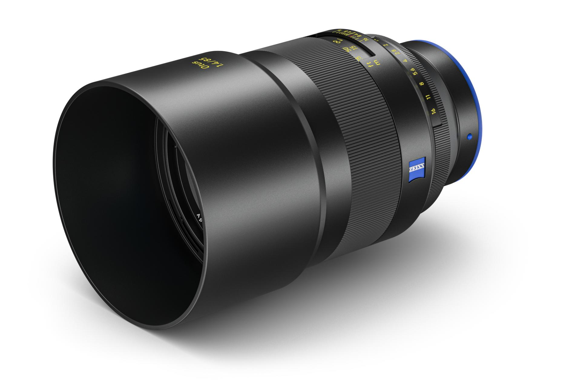 Black ZEISS camera lens with visible focus and aperture rings, blue ZEISS branding, and a lens hood attached.