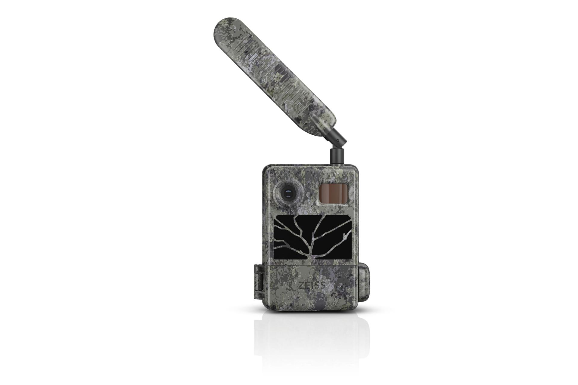Camouflaged ZEISS trail camera with an extended antenna, lens, infrared sensor, and display showing a black-and-white image of tree branches.