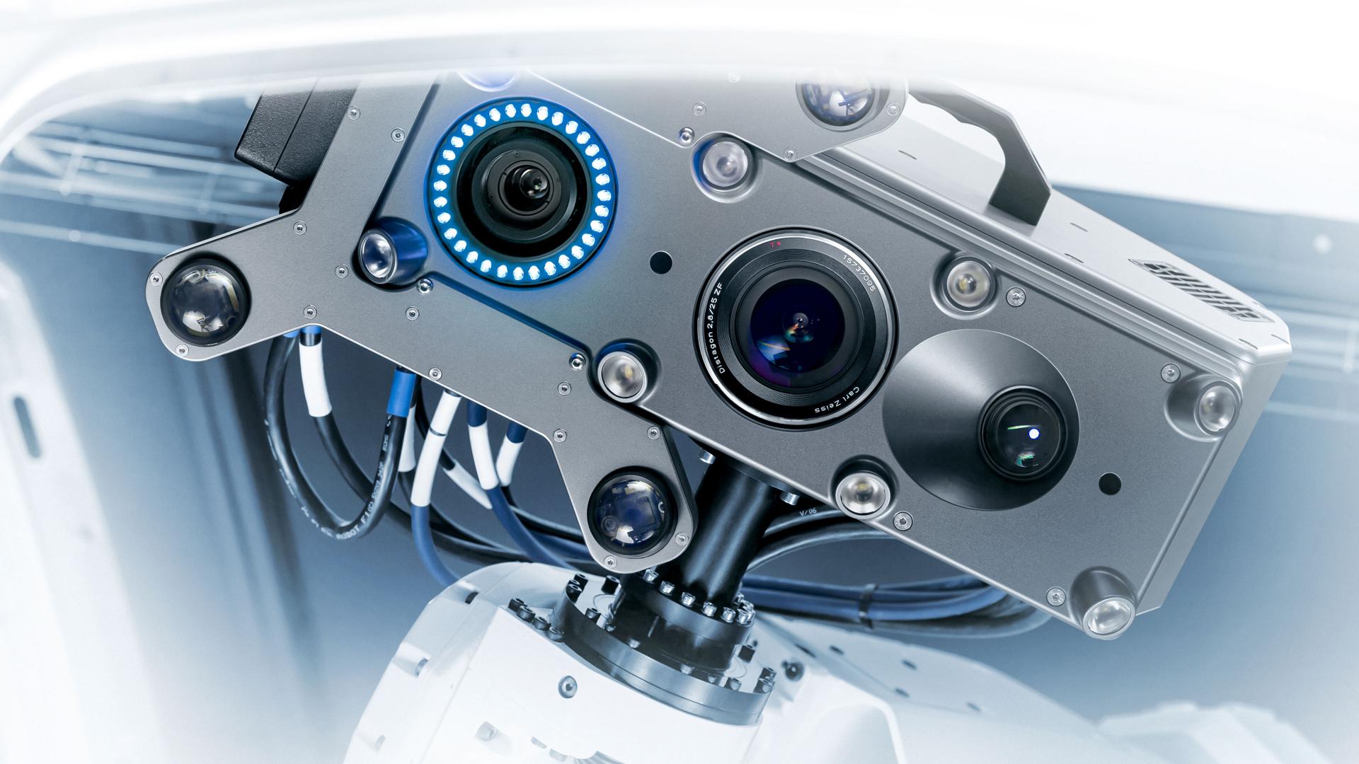 Close-up of a high-precision ZEISS 3D scanning sensor with multiple lenses and LED lights mounted on a robotic arm.