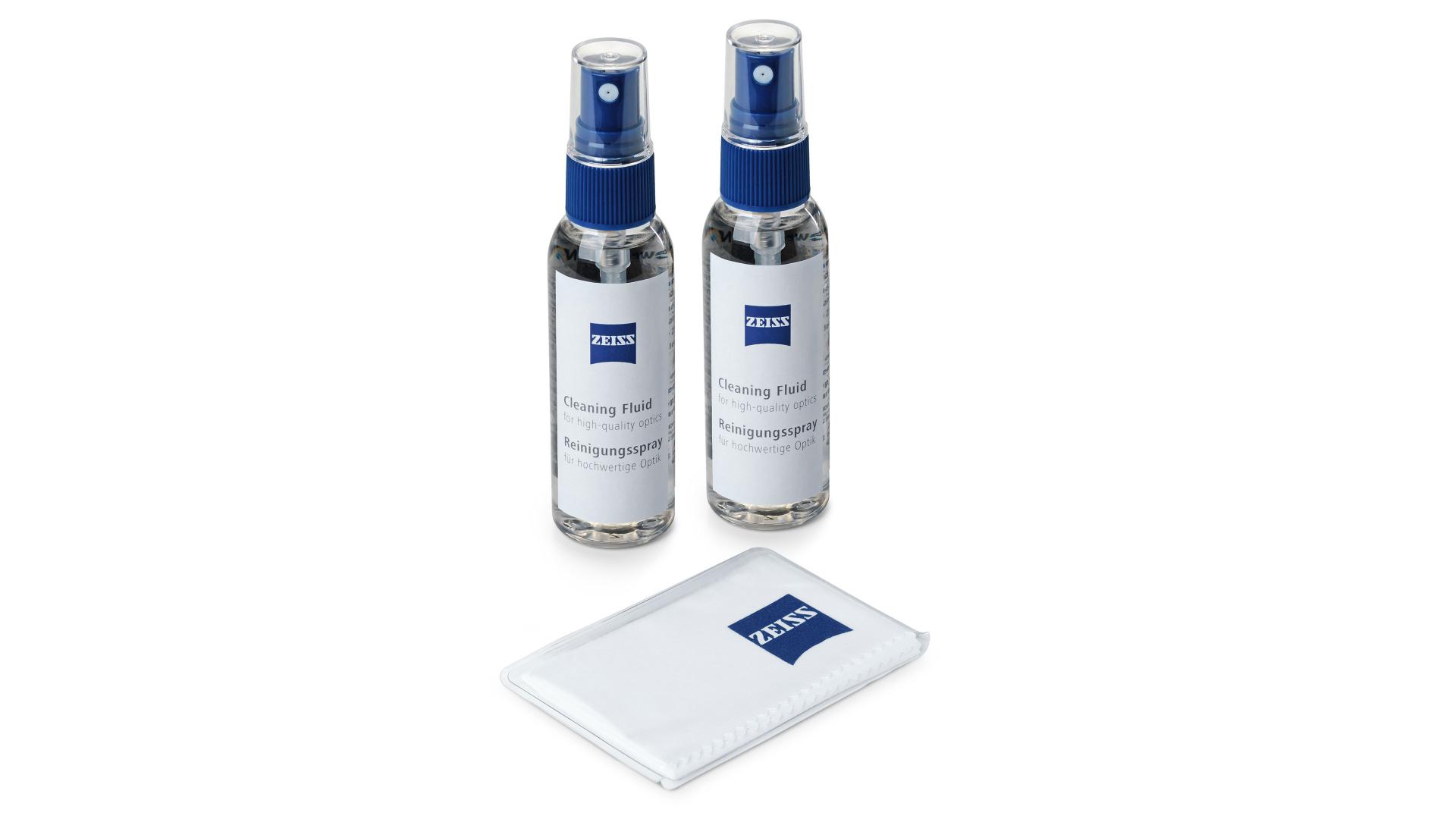 Two ZEISS lens cleaning spray bottles are standing upright behind a folded ZEISS-branded microfiber cleaning cloth.