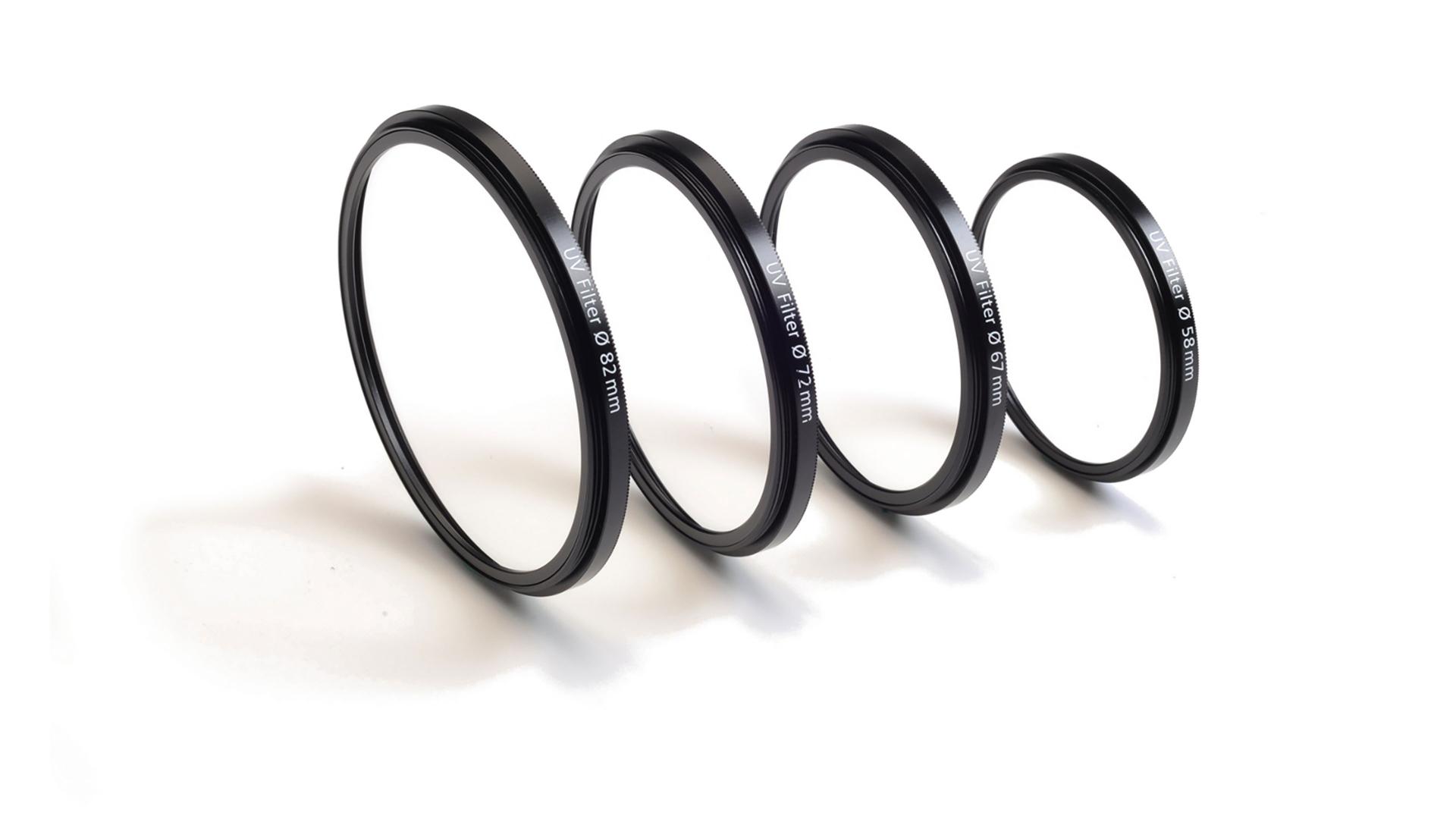 Four ZEISS camera lens filters of varying diameters are standing upright in a row on a white surface.