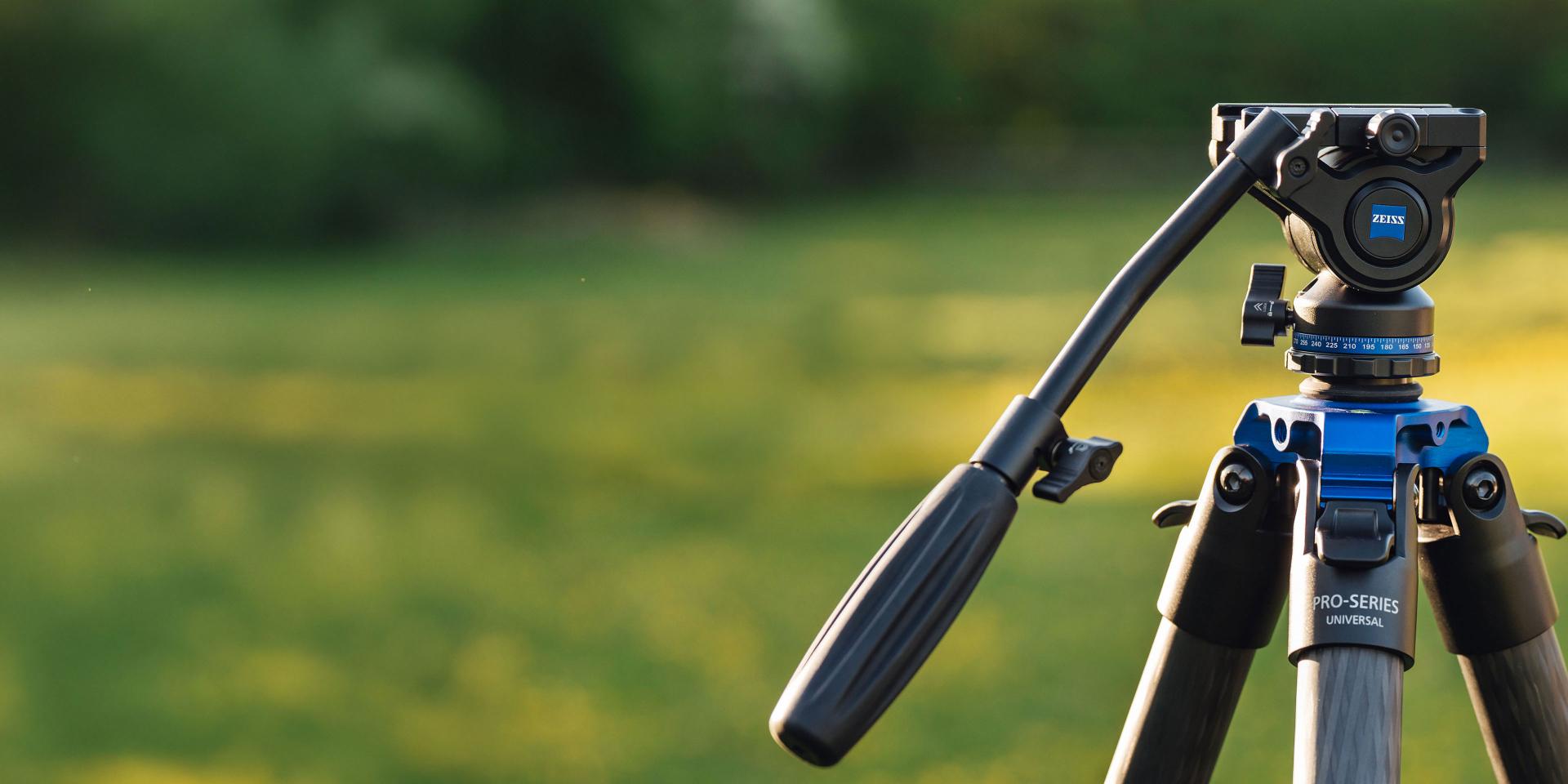 Close-up of a professional tripod head with ZEISS branding set up outdoors on a grassy background.