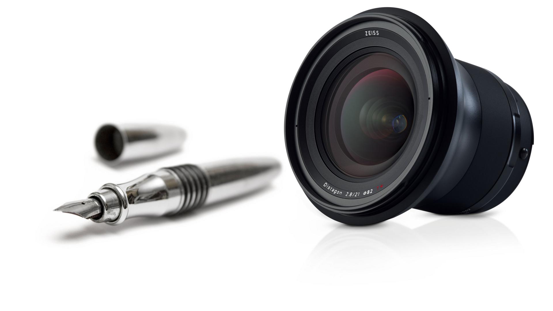 A ZEISS camera lens is displayed next to an uncapped silver fountain pen on a white background.