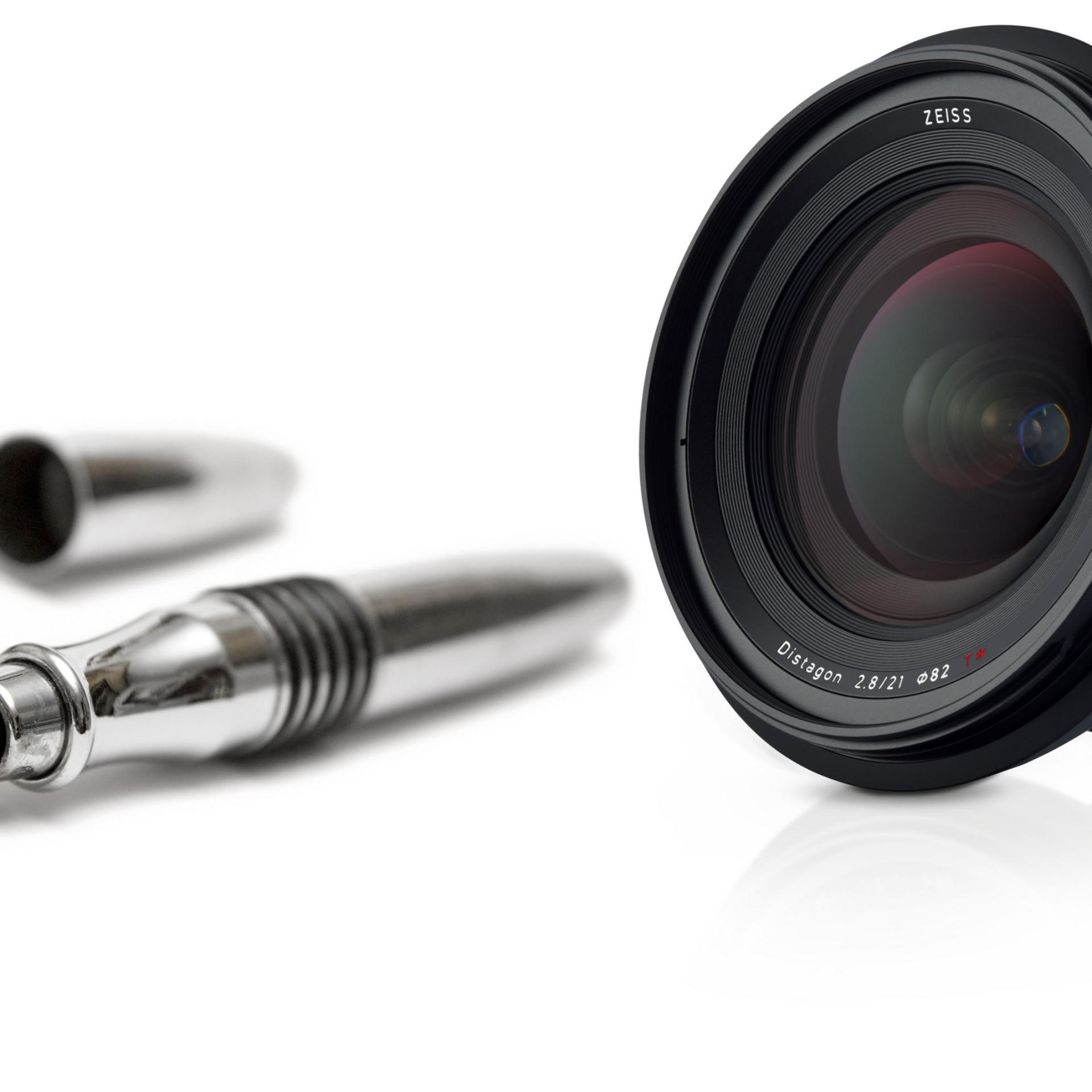 A ZEISS camera lens is displayed next to an uncapped silver fountain pen on a white background.