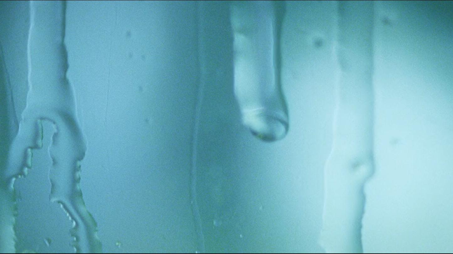 Close-up of condensation and water streaks on a glass surface with a cool blue tint.