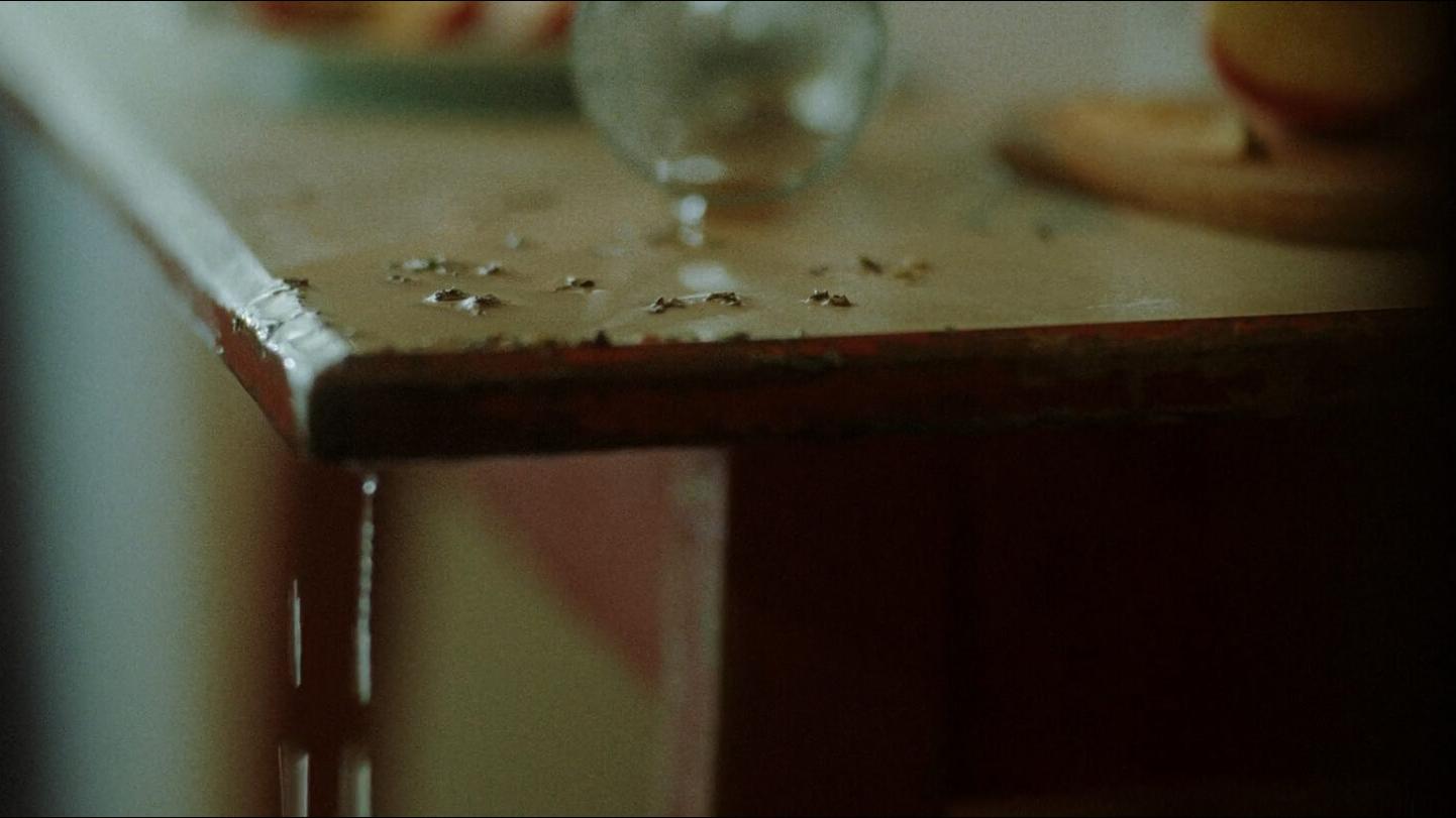 Close-up of a worn table edge with scattered debris and a glass object in soft focus, showcasing fine detail and depth captured with ZEISS optics.