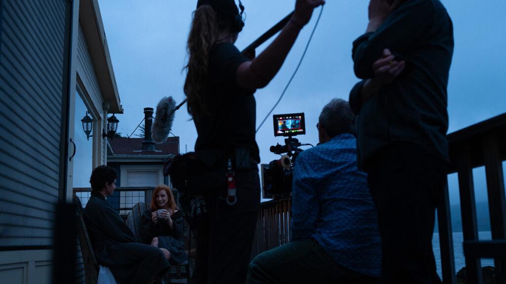 Film crew operating a camera setup on a balcony during a scene shoot, with a ZEISS monitor displaying the shot.