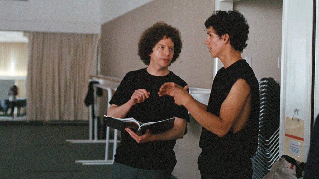 Two people are standing in a spacious room having a focused discussion while looking at an open book.