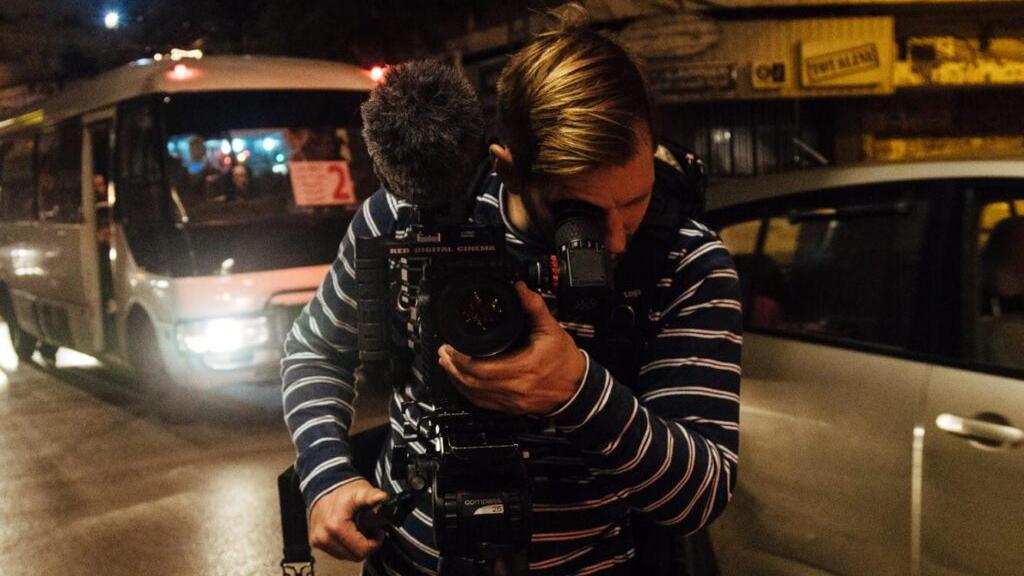 A filmmaker operates a professional camera rig at night on a city street, using a ZEISS lens for high-quality video capture.