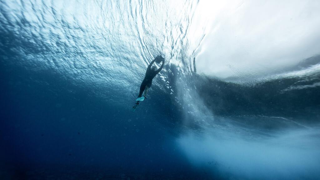 A diver is swimming upwards toward the surface of the ocean, with light filtering through the water above.