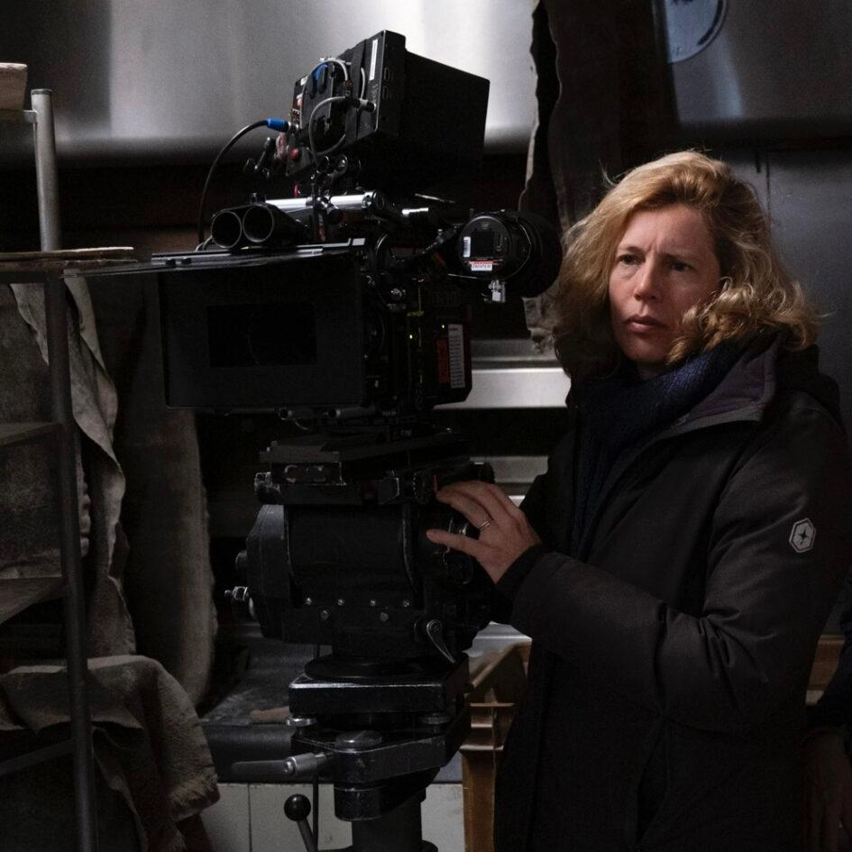 A woman operates a professional cinema camera equipped with ZEISS lenses on a film set.