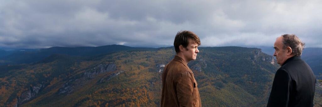 Two men stand on a mountain overlook with a scenic view of forested hills and a cloudy sky captured in sharp detail, illustrating the imaging quality of ZEISS optics.