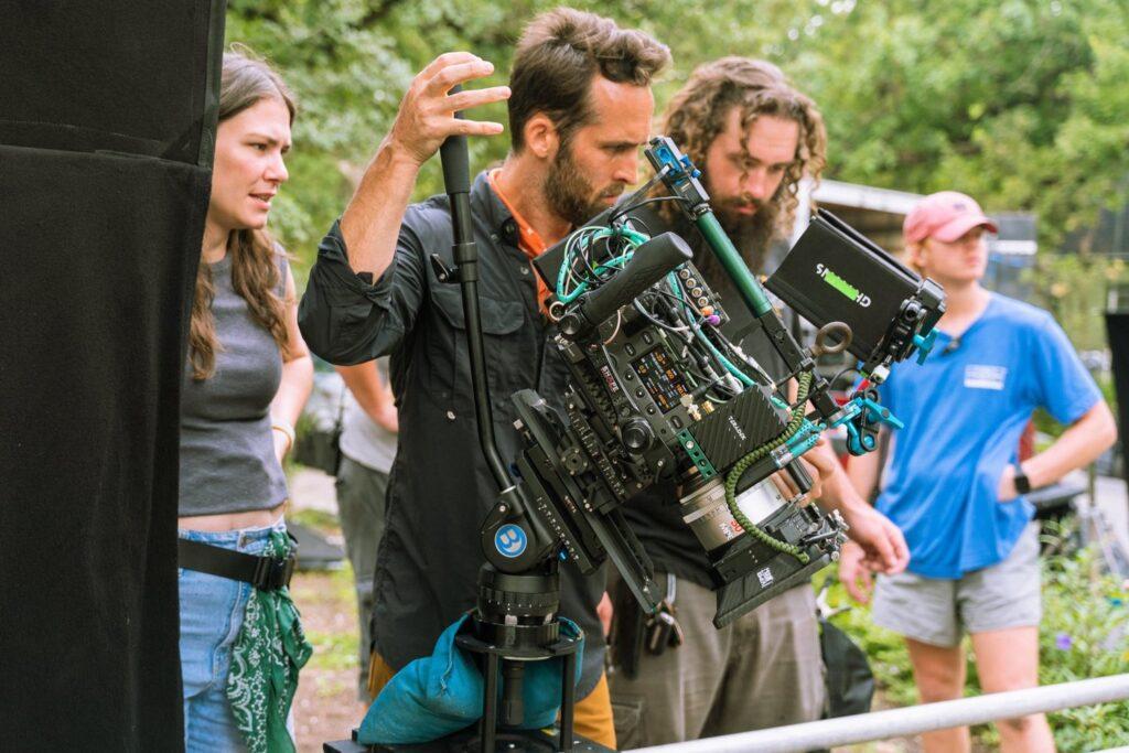 A camera operator films a scene using a professional camera setup equipped with ZEISS lenses in a studio environment.