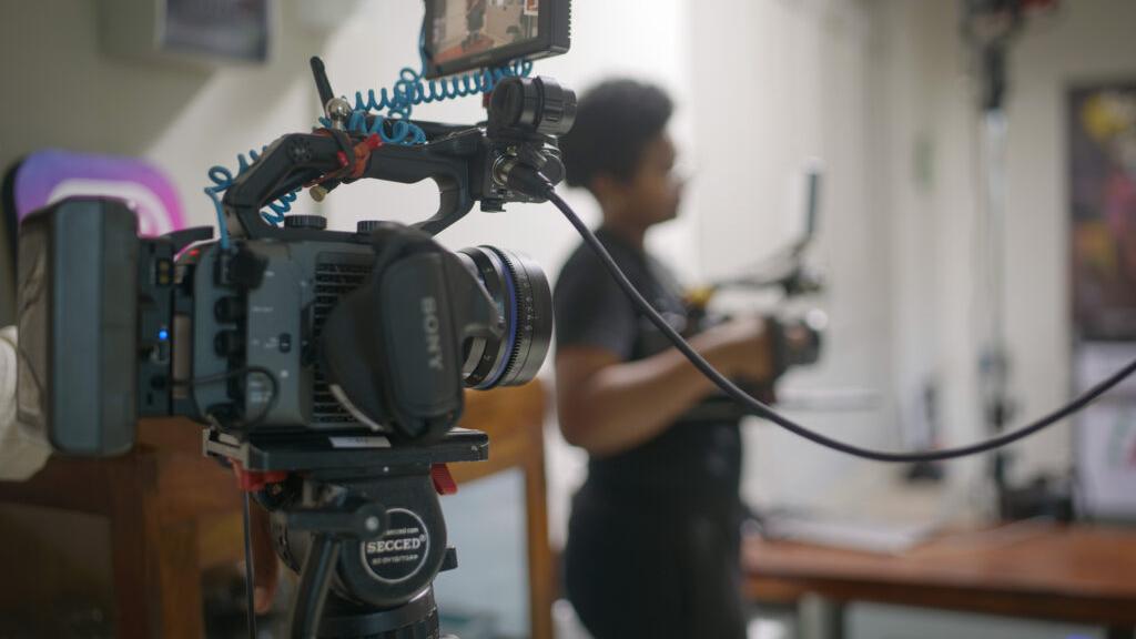 Professional video camera equipped with a ZEISS lens set up in a studio with a person operating another camera in the background.