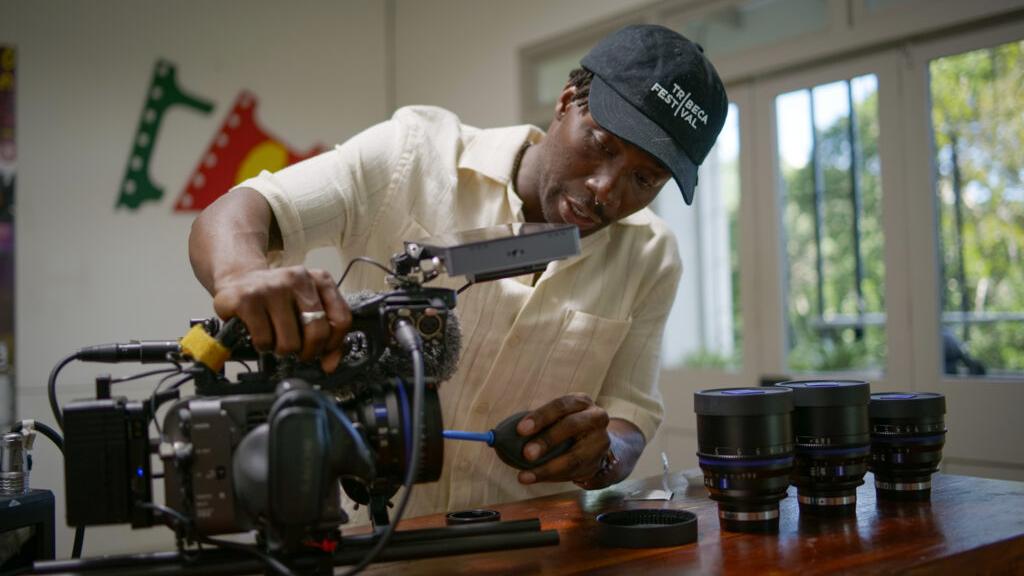 A man is adjusting a professional cinema camera on a table next to several ZEISS camera lenses.