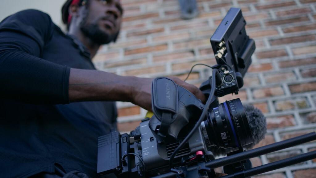 Man operating a professional video camera equipped with a ZEISS lens in an outdoor setting.