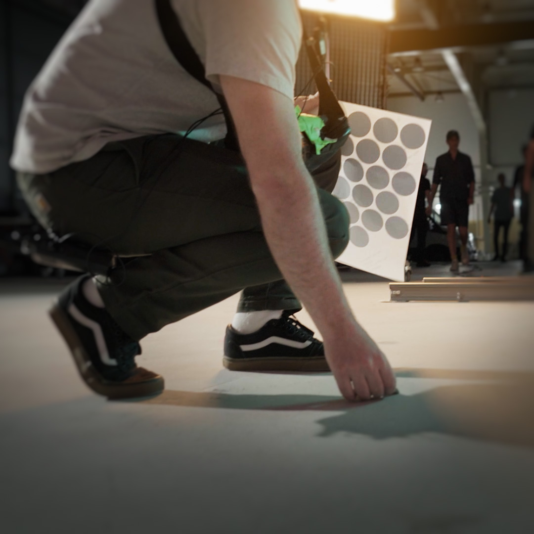 Person crouching on a studio floor with a ZEISS calibration chart in the background during a professional setup.