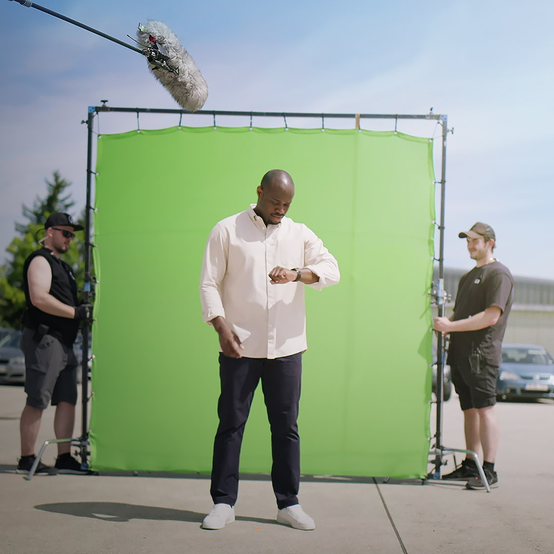 A professional actor standing in front of a green screen on a film set, with a camera crew and boom microphone positioned for a high-quality ZEISS production.