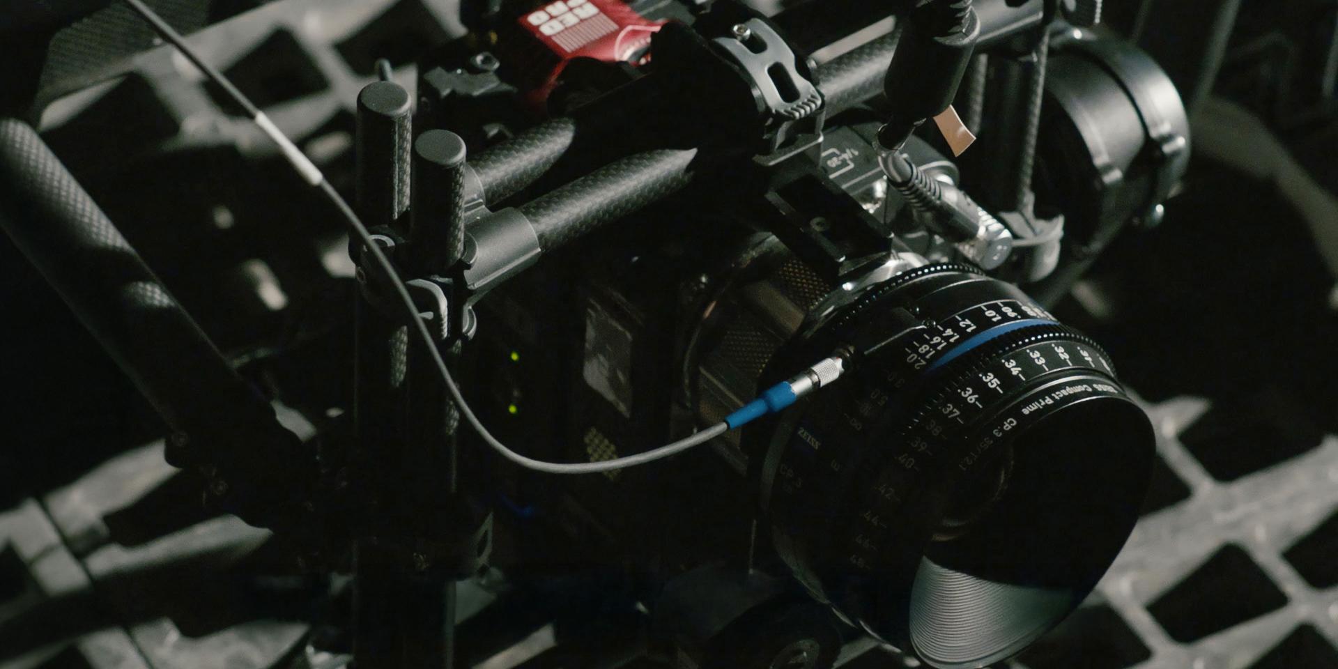 Close-up of a professional cinema camera rig equipped with a ZEISS lens in a dimly lit setting.
