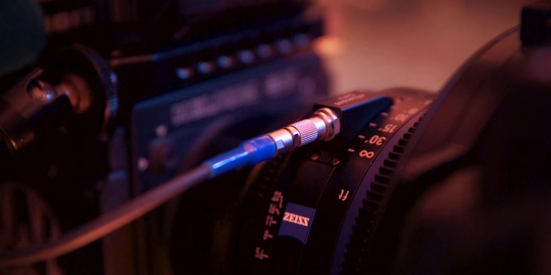 Close-up of a professional camera setup featuring a ZEISS cine lens with a connected control cable.