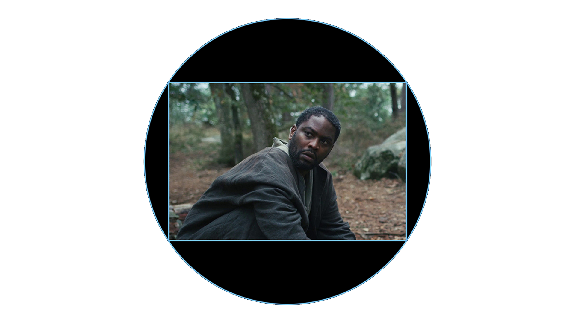 A man in a dark jacket sits on the forest floor surrounded by trees, framed within a circular ZEISS lens view.