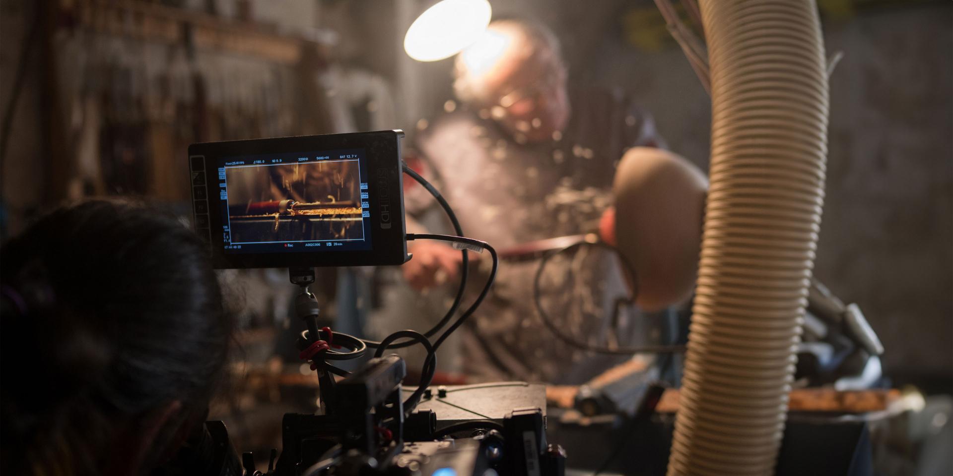 A camera setup with a monitor displaying a close-up of a craftsman woodworking in a dimly lit workshop, captured using ZEISS lenses.