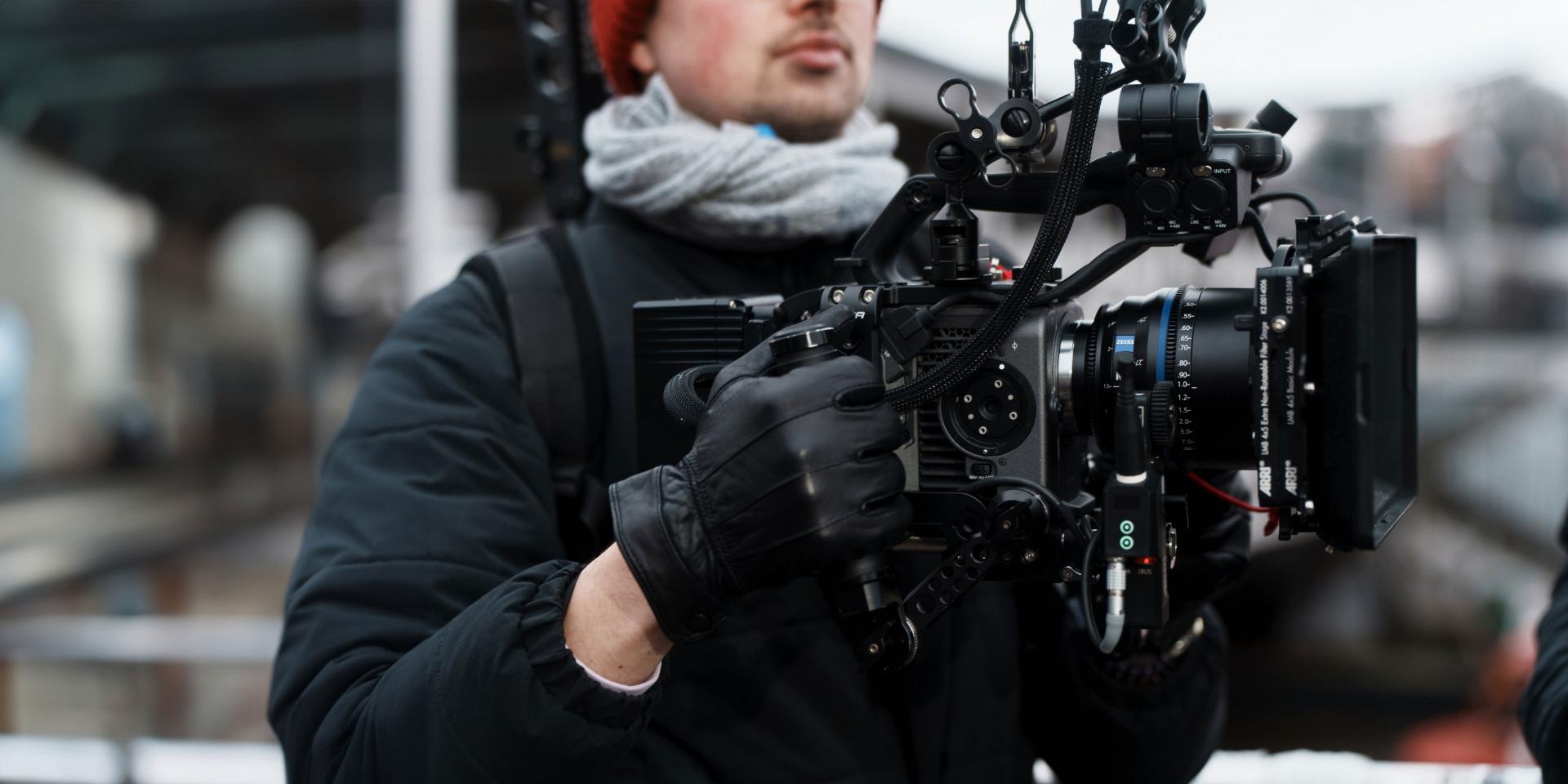 Cinematographer holding a professional camera rig equipped with a ZEISS lens outdoors.