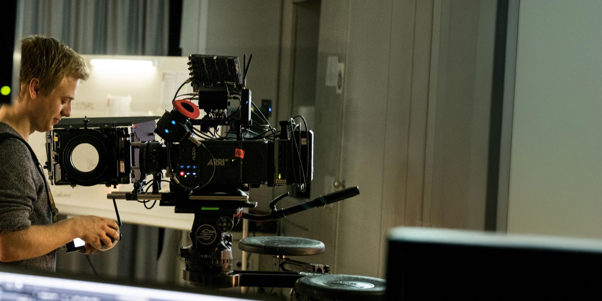A man is operating a professional cinema camera setup equipped with ZEISS lenses in an indoor studio environment.