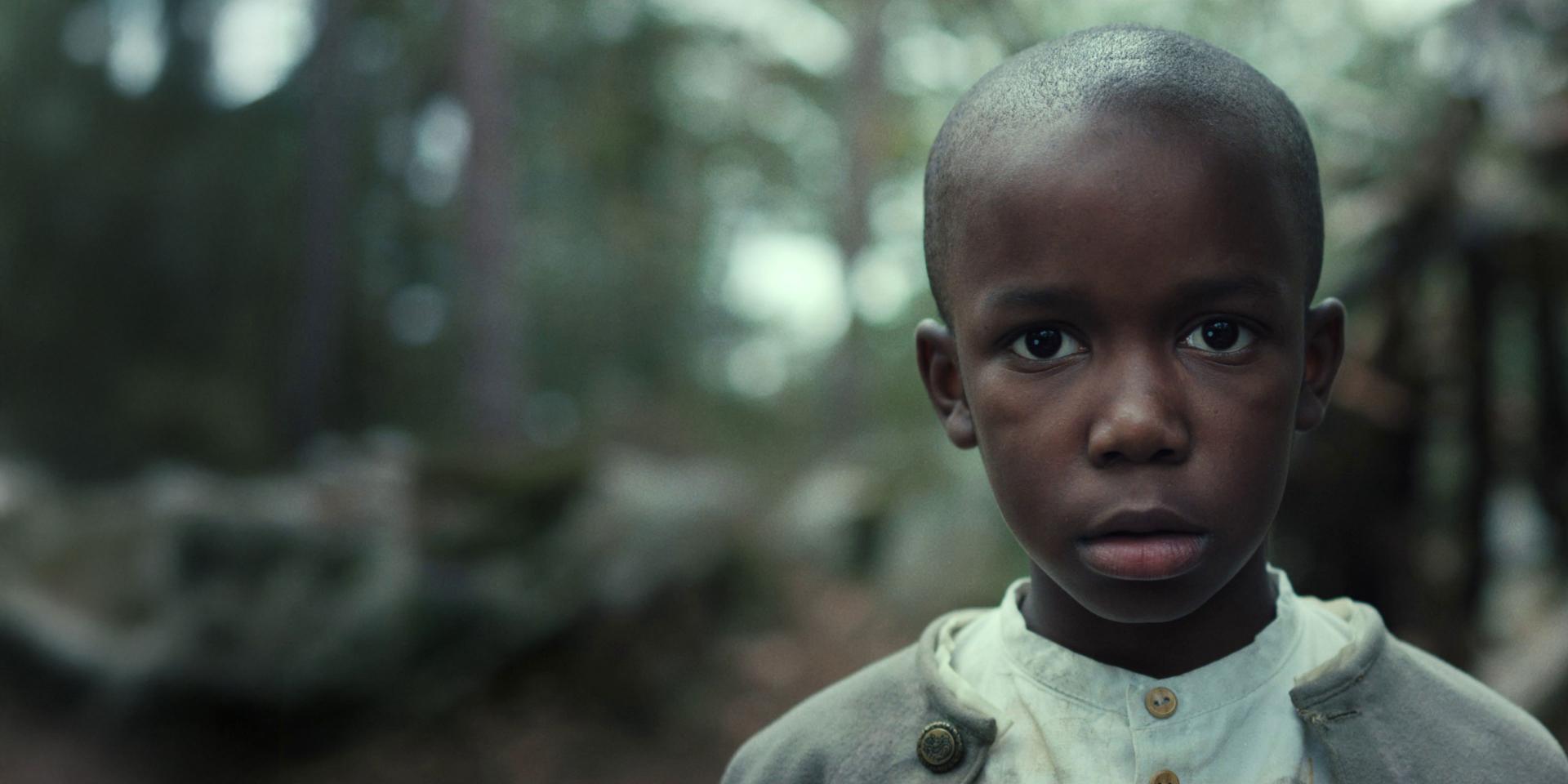 A young boy stands in sharp focus in a forest setting with a soft, blurred background, showcasing the depth of field and clarity achieved with ZEISS optics.