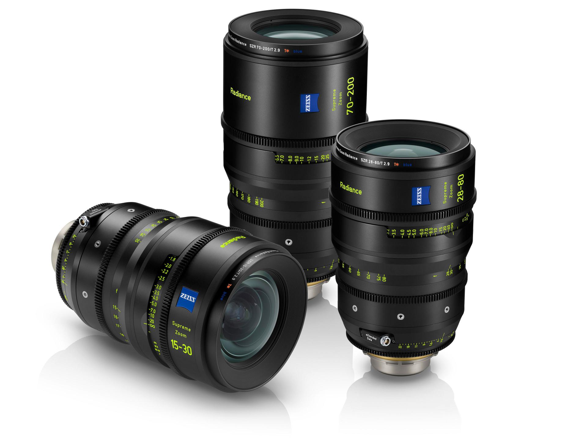 Three black ZEISS Supreme Prime Radiance camera lenses with yellow and white markings are displayed standing and lying on a white background.