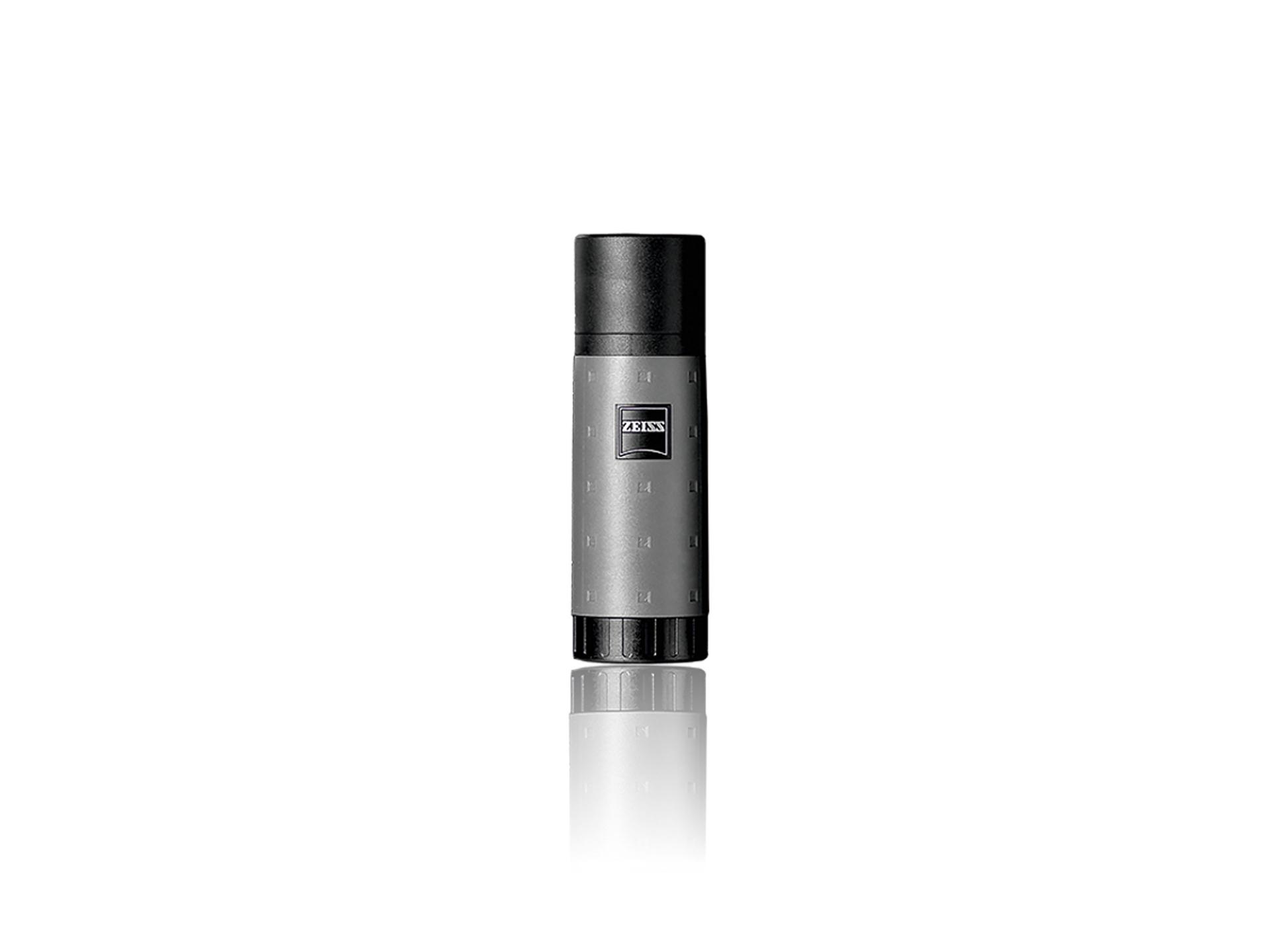 Grey and black cylindrical ZEISS lens cleaning spray bottle standing upright on a reflective white surface.