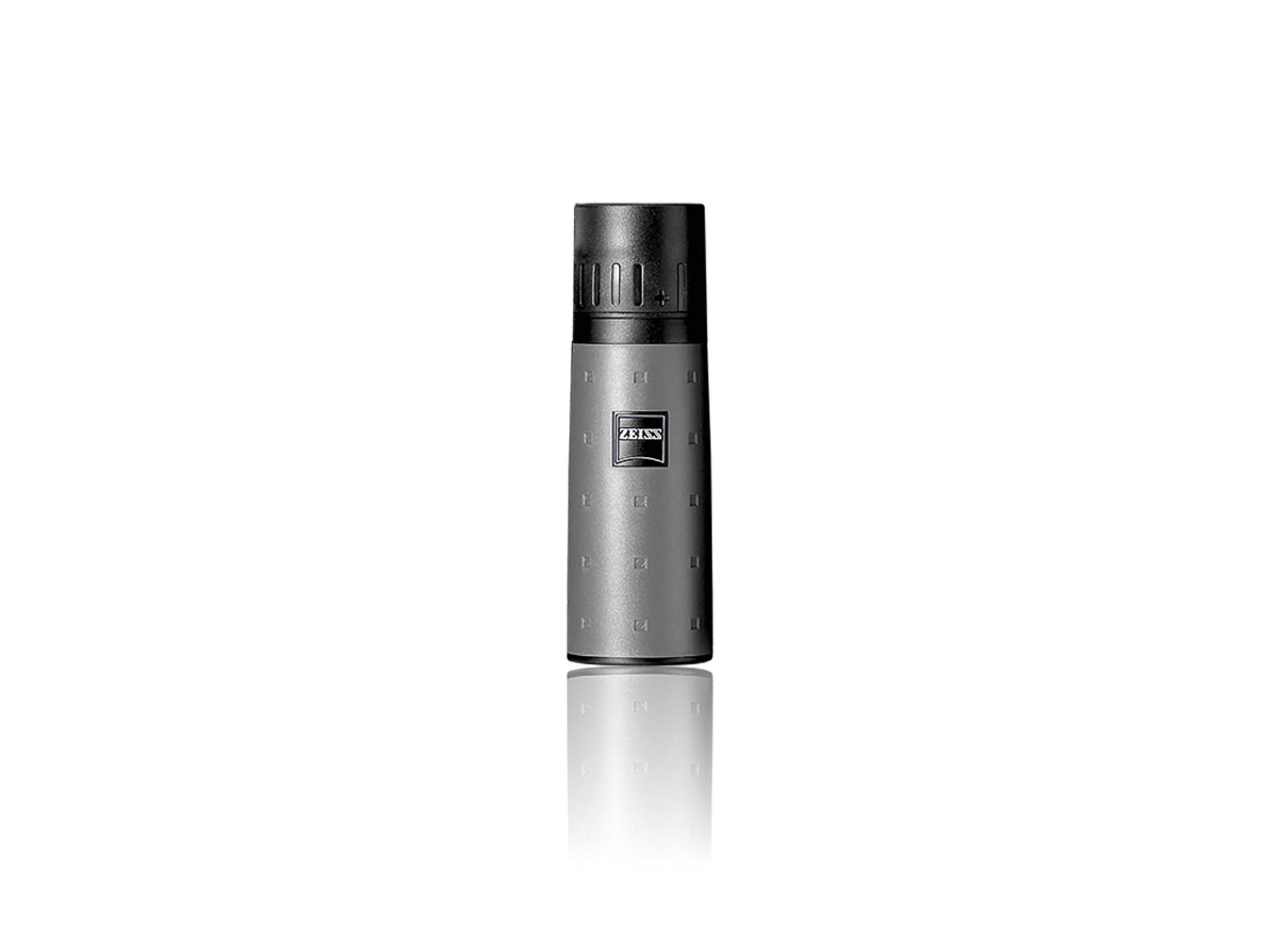 Compact, cylindrical ZEISS monocular with a textured grey body and black top, standing upright on a white reflective surface.