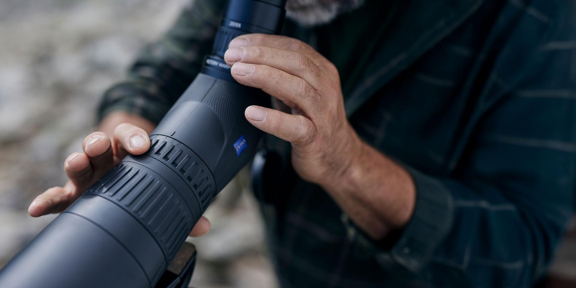 A person adjusts the focus ring on a ZEISS spotting scope in an outdoor setting.