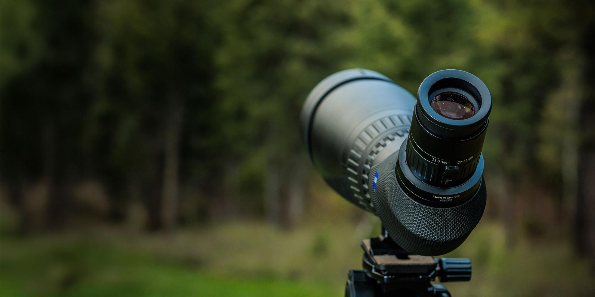 Close-up of a ZEISS spotting scope mounted on a tripod with a blurred forest background.