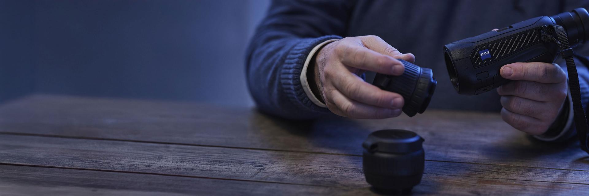 A person is assembling a ZEISS camera lens system on a wooden table.