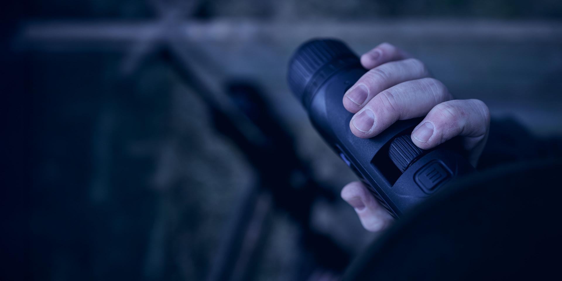 A person holding a ZEISS thermal imaging monocular in a dim outdoor setting.