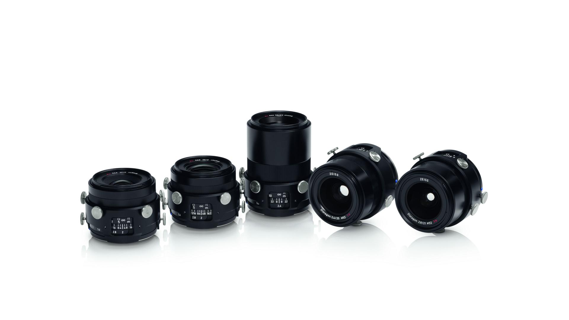 Five professional ZEISS camera lenses are displayed in a row on a white reflective surface.