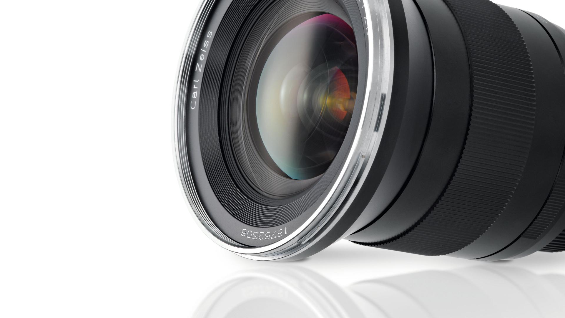Close-up of a ZEISS camera lens with visible glass elements and detailed lens markings on a white reflective surface.