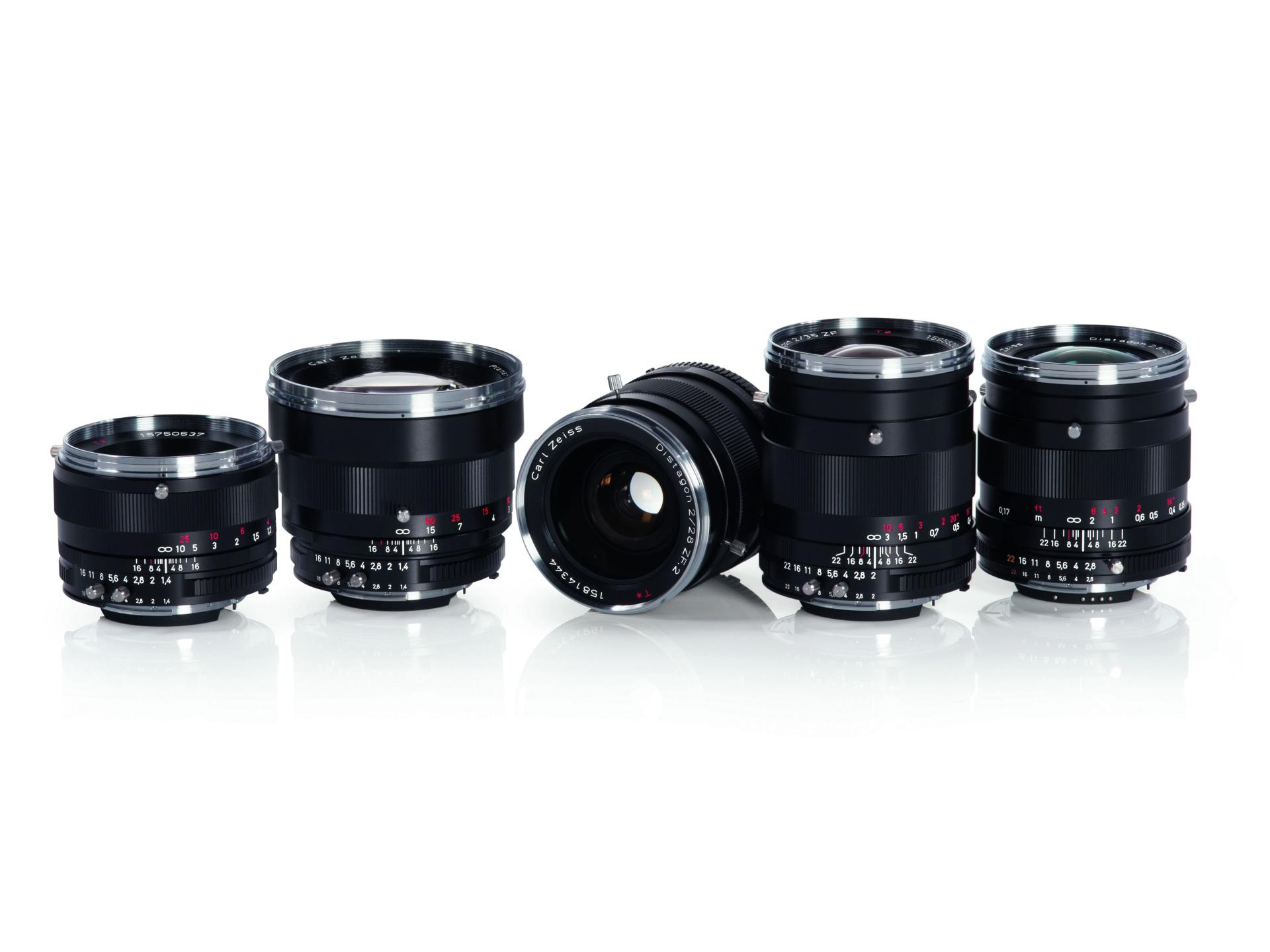 Five black ZEISS camera lenses are arranged in a row on a reflective white surface.