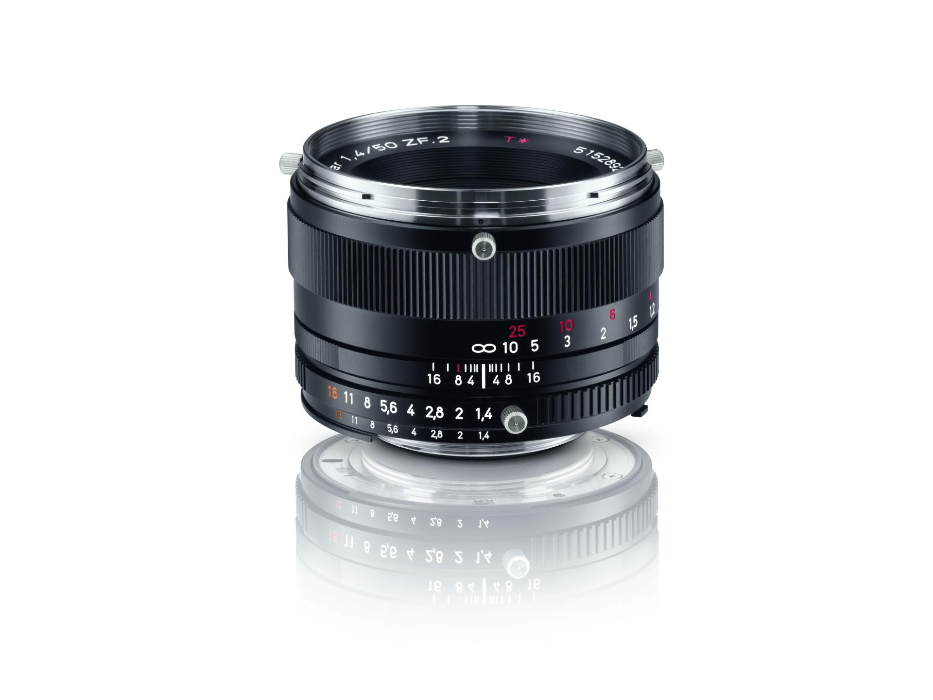A black ZEISS camera lens with detailed aperture and focus markings, displayed upright on a white reflective surface.