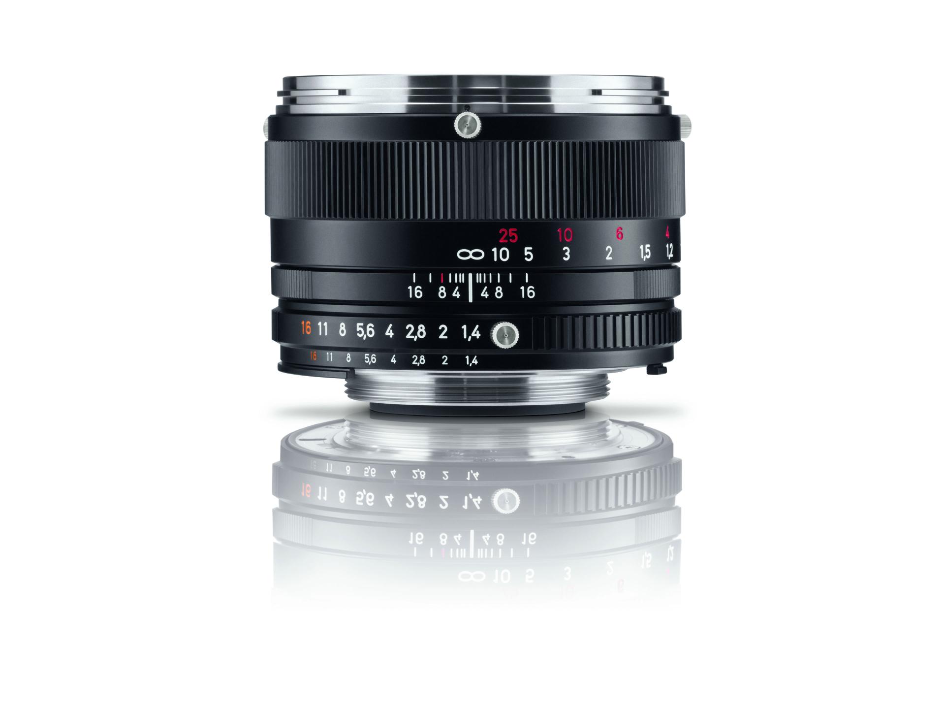Black ZEISS camera lens with focus and aperture markings, displayed upright with a reflection beneath it on a white background.