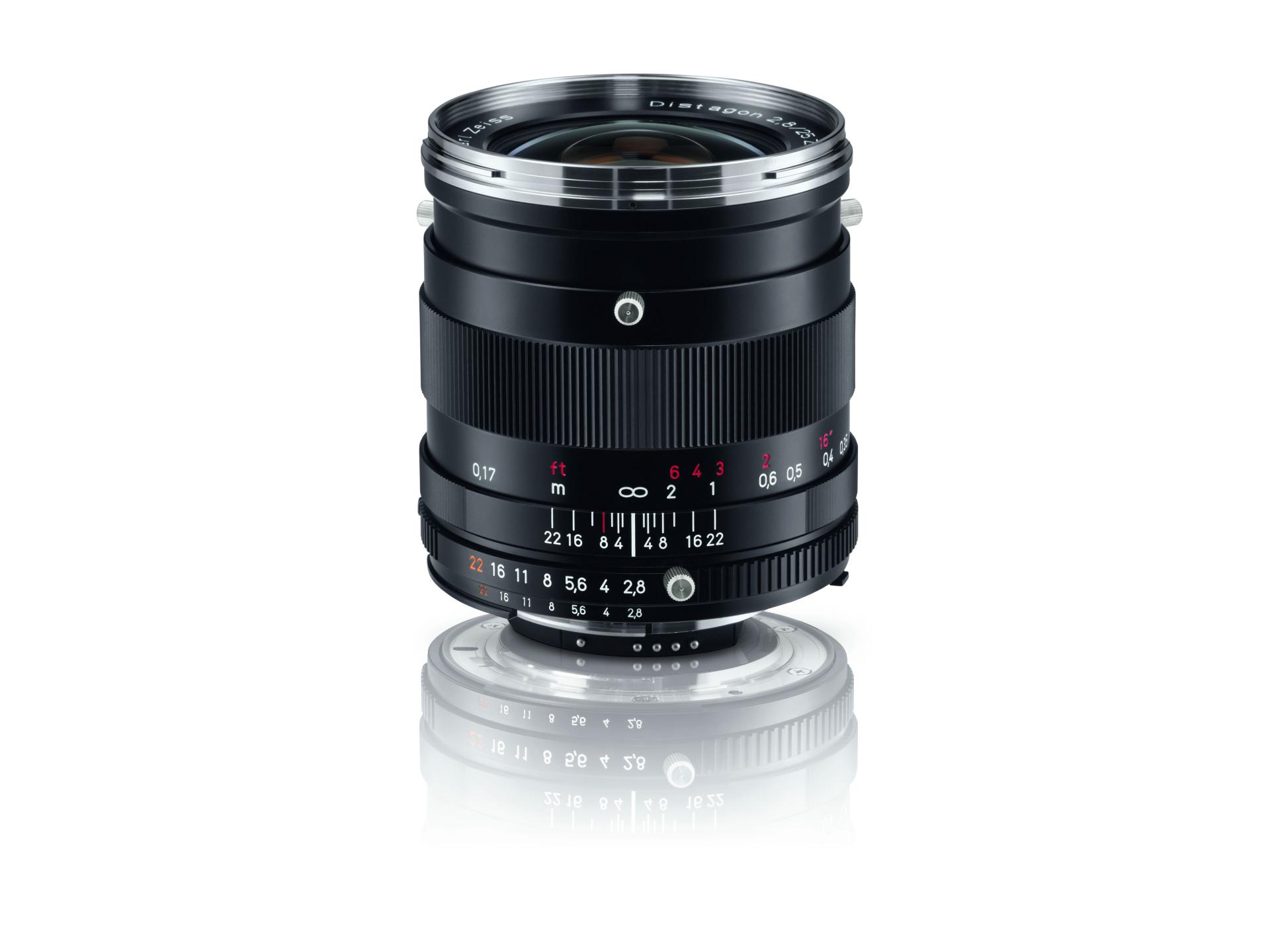Black ZEISS camera lens with manual focus and aperture markings, standing upright on a reflective surface.