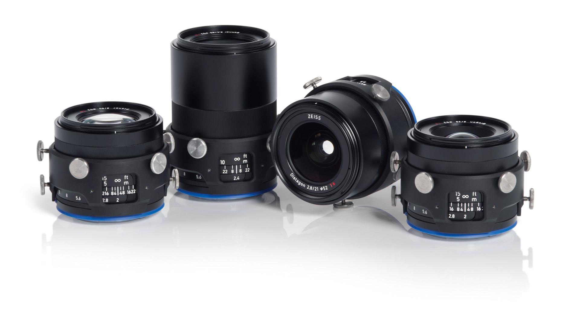 Four professional ZEISS camera lenses with blue accents are displayed upright and at an angle on a white background.