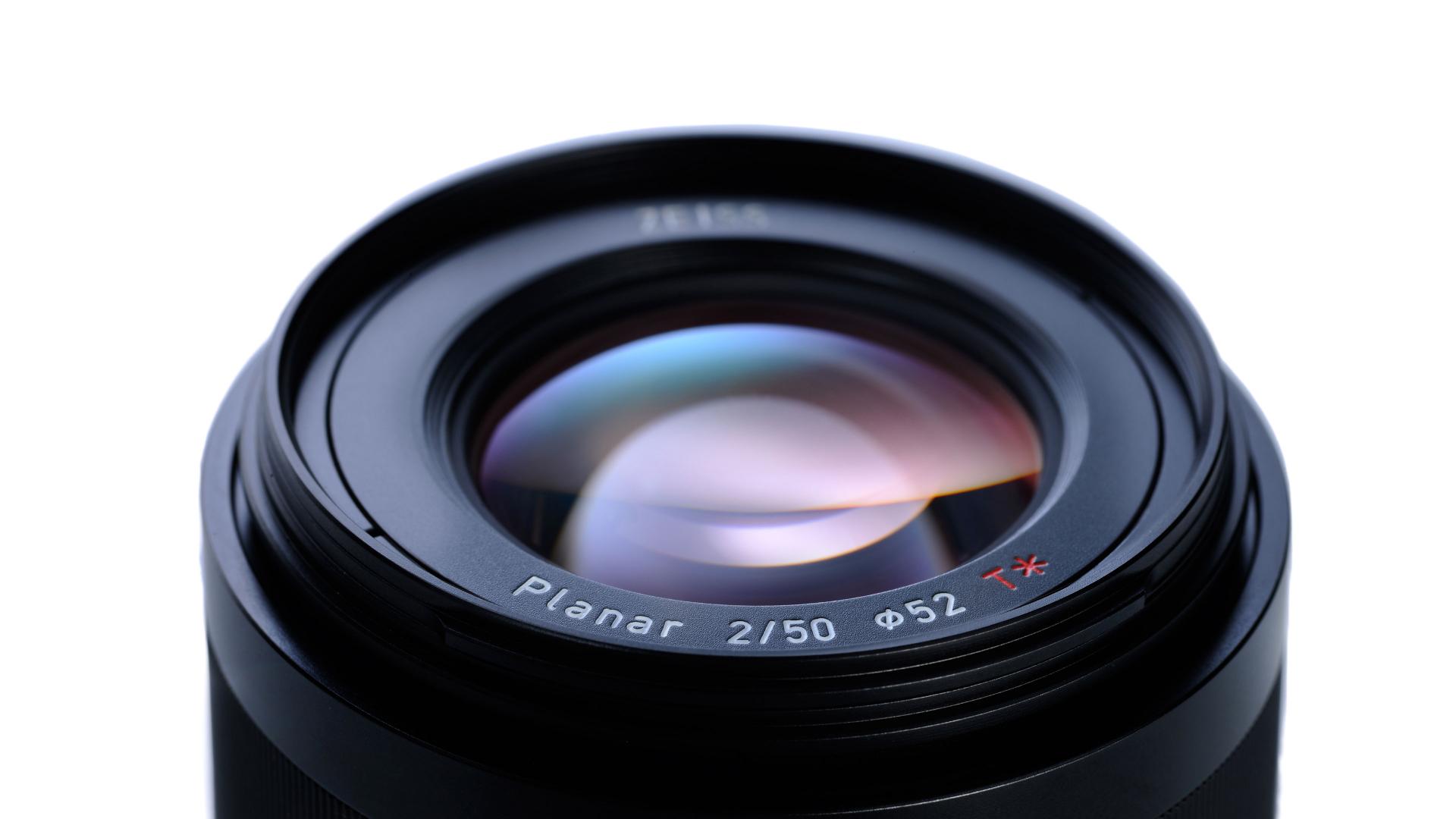 Close-up image of a ZEISS Planar 2/50 camera lens with visible glass elements and engraved labeling.