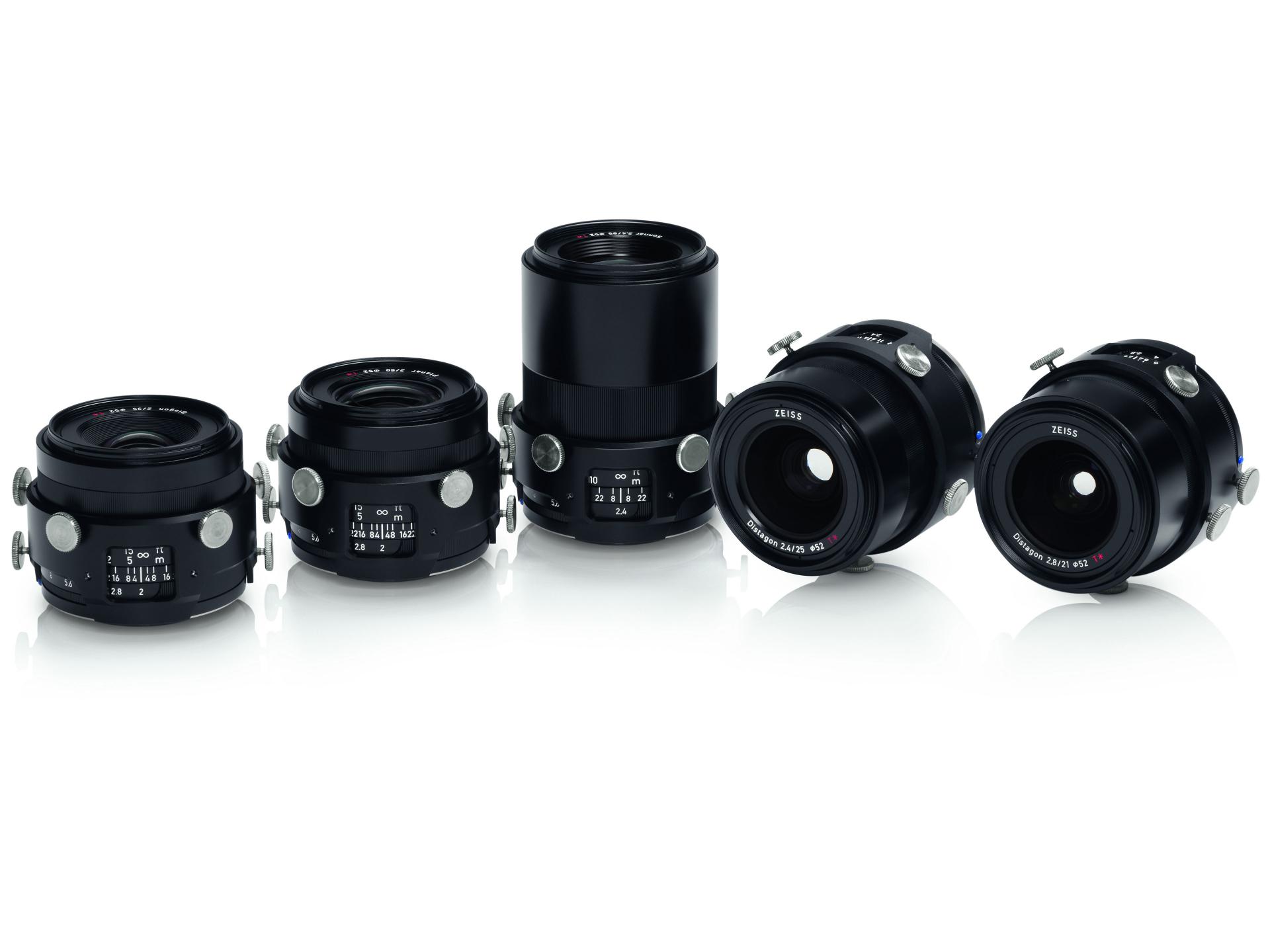 Five professional ZEISS camera lenses are displayed in a row on a white reflective surface.