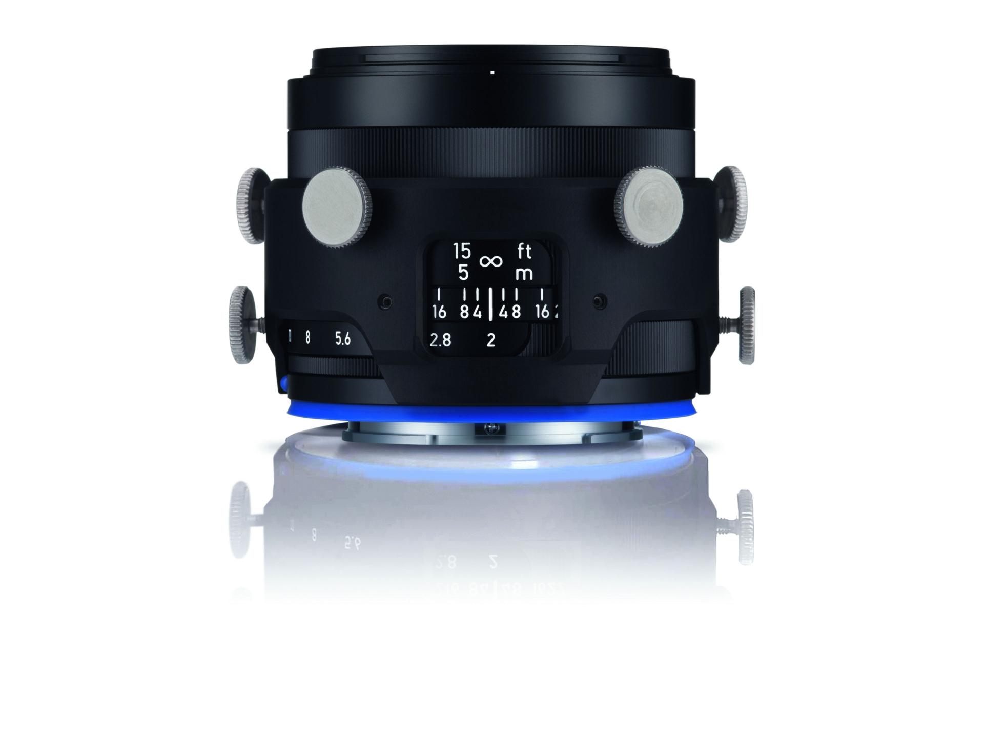 Professional close-up image of a ZEISS camera lens with focus and aperture markings, adjustment knobs, and a blue illuminated base on a reflective surface.