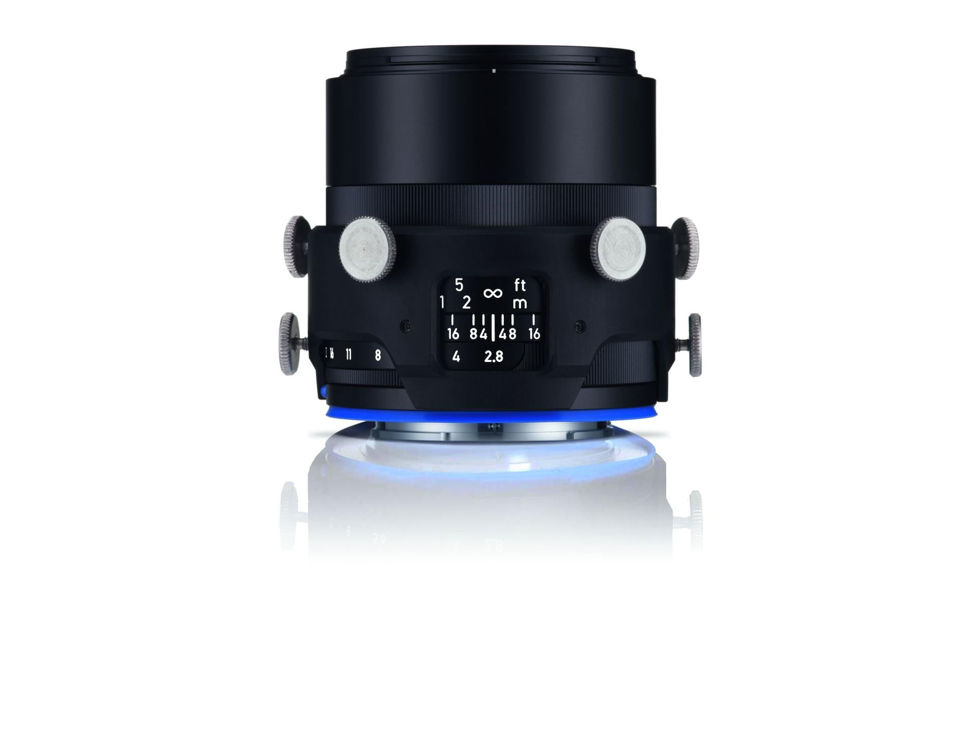 Black professional camera lens with white adjustment knobs and distance scale markings, displayed on a reflective surface with a blue light glow underneath.